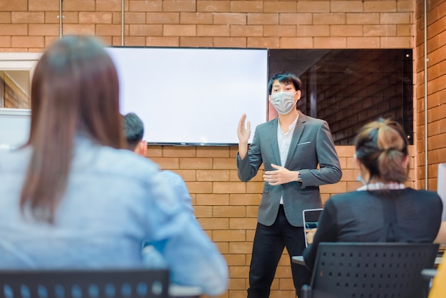 Business cooperation : Young asian male coach or speaker make flip chart presentation to diverse businesspeople at meeting in office. Male tutor or trainer present project to diverse colleagues.