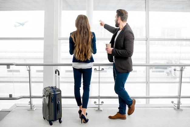 Business couple standing together with baggage near the window at the departure area at the airport