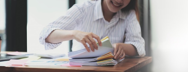 Business Documents concept Employee woman hands working in Stacks paper files for searching and checking unfinished document achieves on folders papers at busy work desk office Soft focus