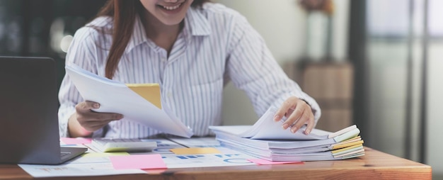 Business Documents concept Employee woman hands working in Stacks paper files for searching and checking unfinished document achieves on folders papers at busy work desk office Soft focus