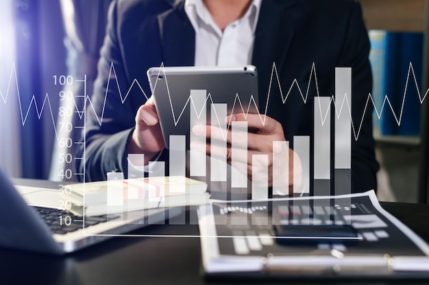 Business documents on office desk with laptop and smart phone and graph business diagram and man working in morning light