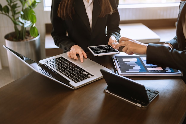 Business documents on office table with smart phone and calculator digital tablet and graph business with social network diagram and two colleagues discussing data working in the office