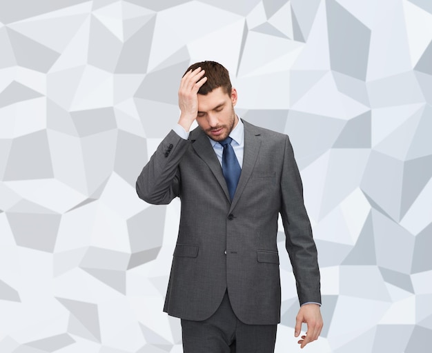 business, education, stress and fail concept - handsome businessman having headache over gray graphic low poly background