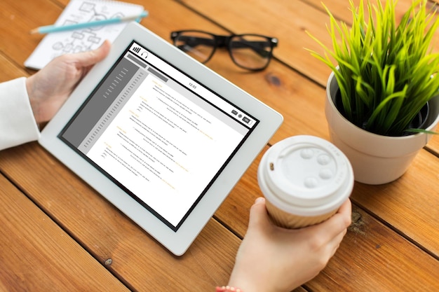 business, education, technology, people and programming concept - close up of woman with coding on tablet pc computer screen and coffee cup on wooden table