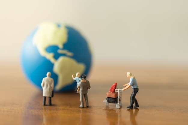 Business, Family Travel Concept. Group of businessman, father and child and male with airport luggage trolley miniature figures people looking to mini world ball on wooden table and copy space.