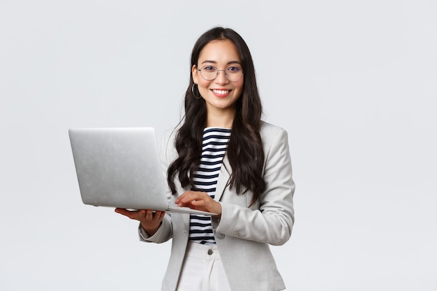 Business, finance and employment, female successful entrepreneurs concept. Confident smiling asian businesswoman, office worker in white suit and glasses using laptop, help clients