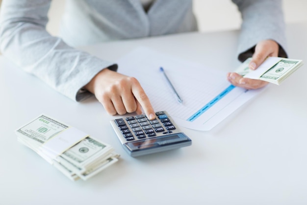 business, finance, tax and people concept - close up of woman hands counting us dollar money with calculator