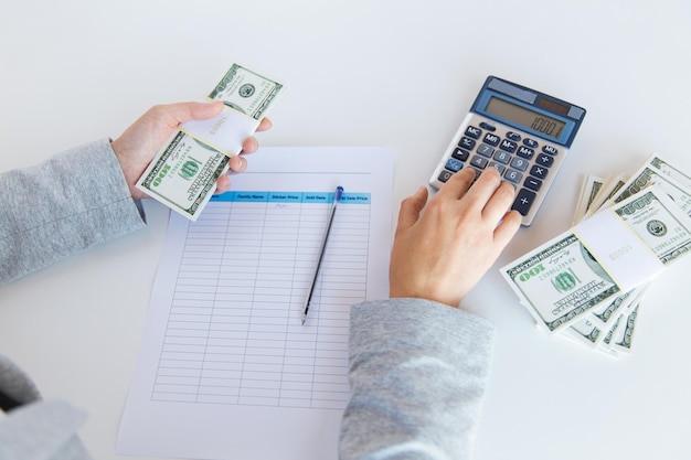 business, finance, tax and people concept - close up of woman hands counting us dollar money with calculator