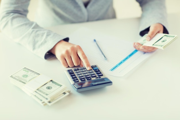 business, finance, tax and people concept - close up of woman hands counting us dollar money with calculator