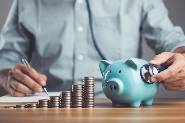 Business Financial and money check up idea Check about health of financial Man using stethoscope to check on piggy bank increasing coin stacked on the table