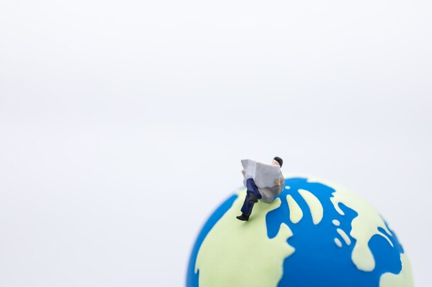 Business, Global and Education . Close up of businessman miniature figure sitting and reading a newspaper on mini world ball.