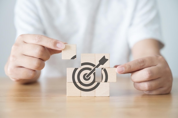 Business goal and ambition to success concept Focus on a goal and achieve successful business Hand holding wooden cube with dart board target aiming icon