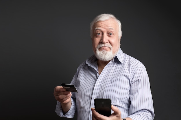 Business, gray-haired man holding a bank card and phone and looks surprised