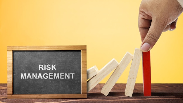 Photo business hand stopping a falling wooden dominoe with risk management text on the chalkboard