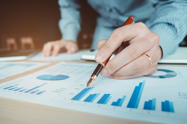 Business hand with a pen pointing on the business paper. Report chart