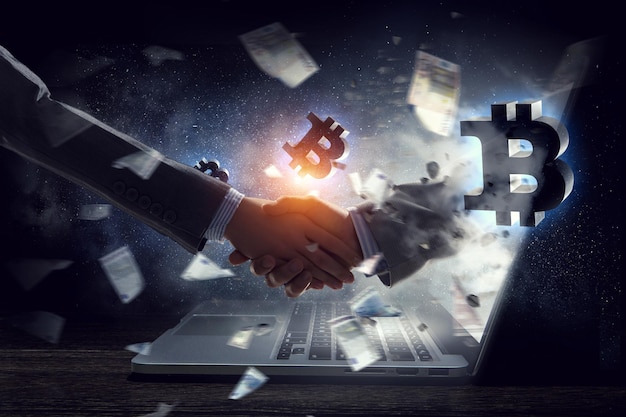 Business handshake by a man and a woman, laptop and bitcoin symbols. Mixed media