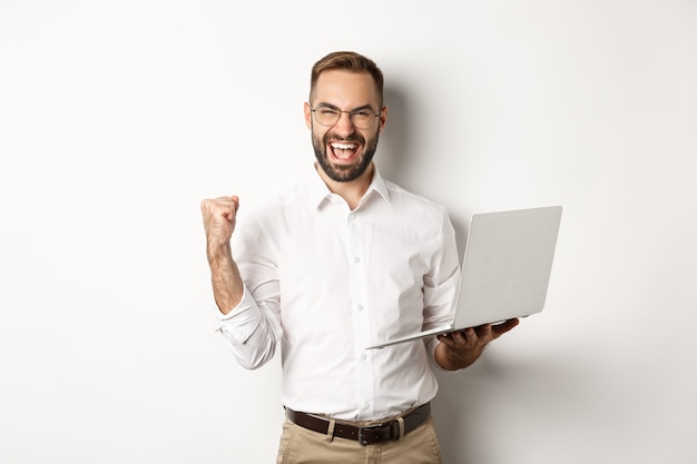 Business. Happy manager winning online, rejoicing with fist pump, holding laptop and triumphing, standing over white background.