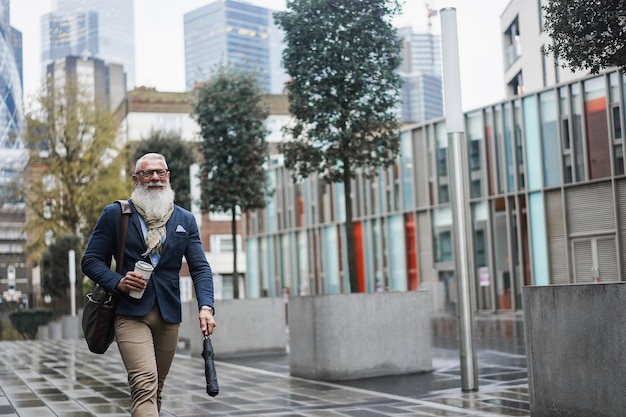 Business hipster senior man walking to work with city in background - Focus face