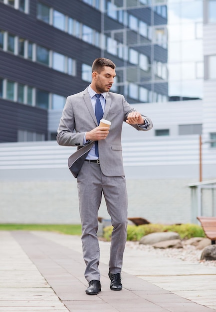 business, hot drinks and people and concept - young serious businessman with paper coffee cup over office building