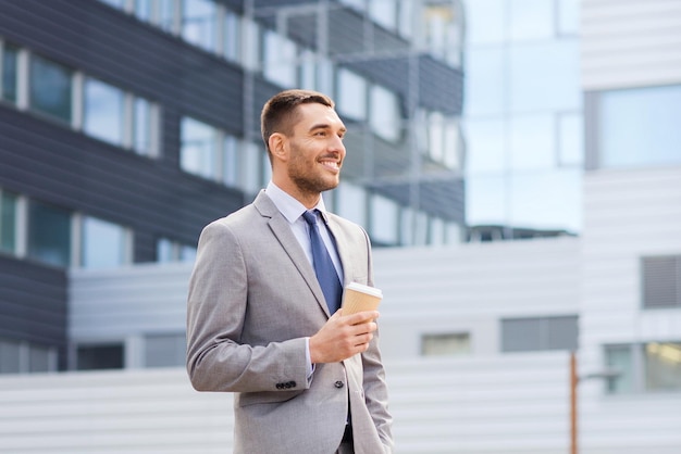 business, hot drinks and people and concept - young serious businessman with paper coffee cup over office building