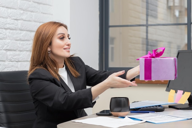 Business ladies sitting behind the desk and accepting present box