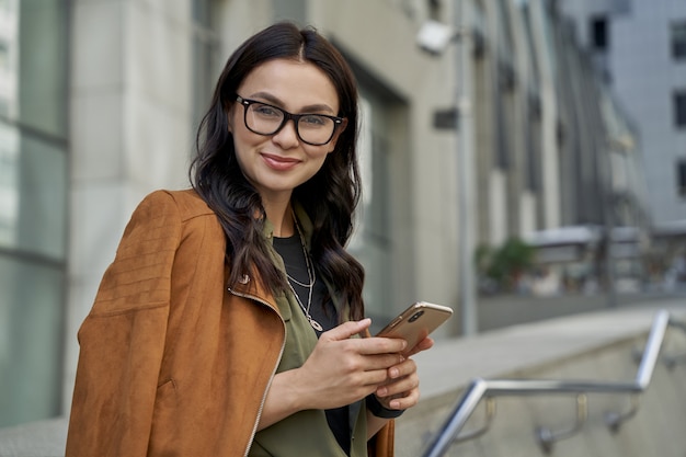 Business lady portrait of a young beautiful happy caucasian woman holding her smartphone and smiling