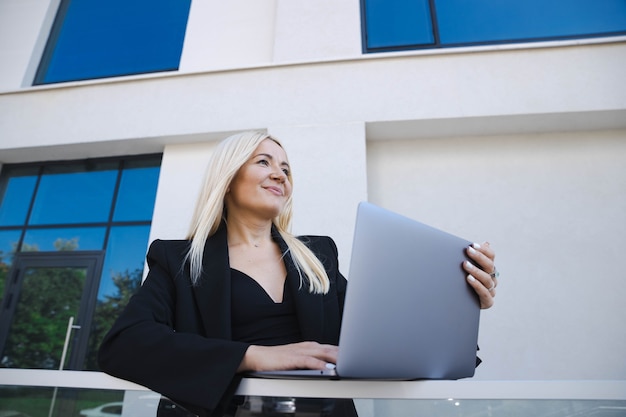 A business lady in a stylish suit is working at a laptop on the street