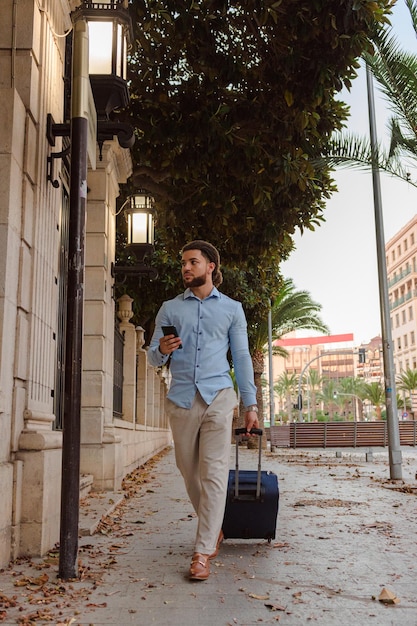 Business latin man with a suitcase and a mobile phone on the street