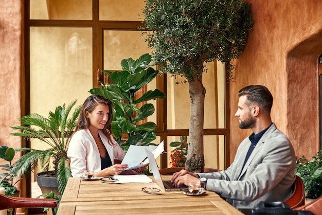 Business lunch man sitting at table working on laptop at restaurant while woman reading documents