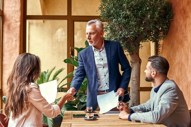 Business lunch three people in the restaurant sitting at table making deal senior man shaking