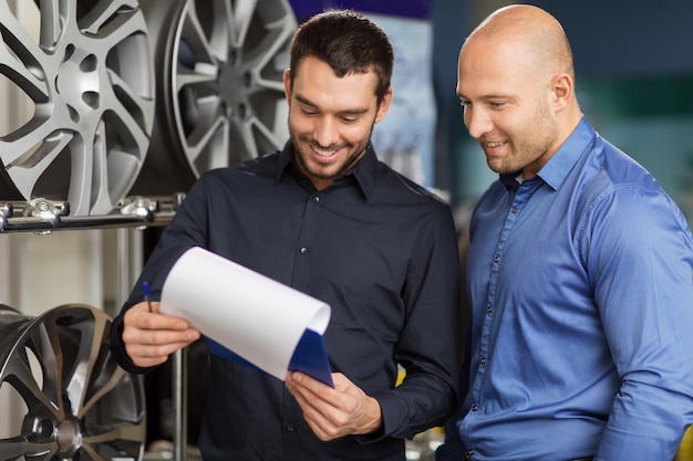 Photo business maintenance and people concept male customer choosing alloy wheel rims and salesman with clipboard at car repair service or auto store