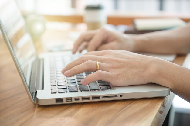 Business male hands typing on a laptop keyboard on desk with a cup of coffee in evening.