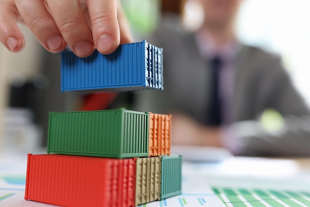 Business man arranging stack of freight cargo containers on office desk with financial documents