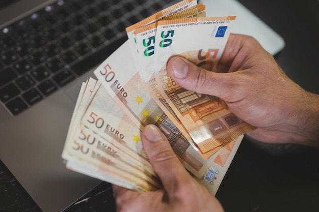 Business man counting money. rich male hands holds and count cash banknotes of 50 euros bills or notes currency in front of a laptop