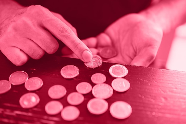 Business man counting money rich male hands holds and count coins of different euros on table toned in viva magenta trend color of the year 2023