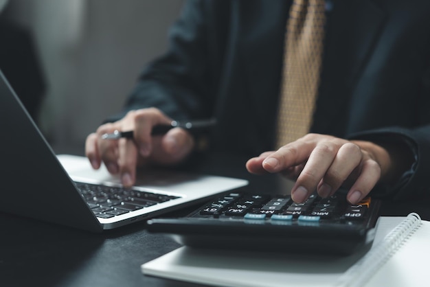 Business man hand using calculator holding pen and with doing finance and tax accounting on desk at home office