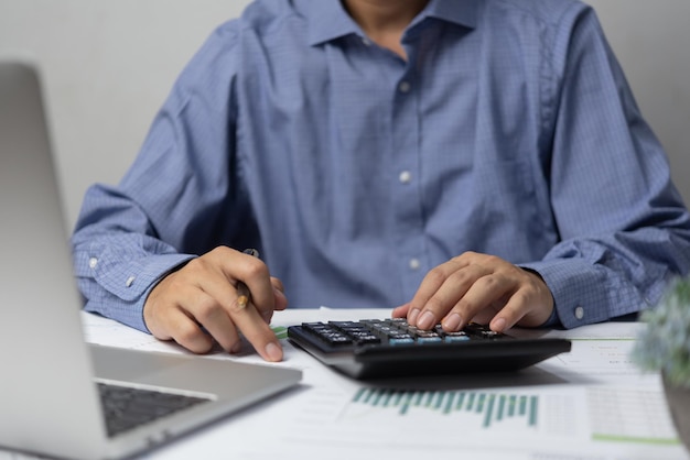 Business man hand using calculator holding pen and with doing finance and tax accounting on desk at home office