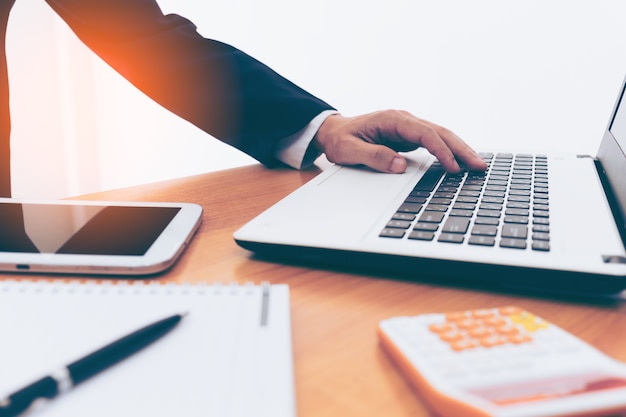 business man hands on laptop with tablet, phone and cup of coffee in a office