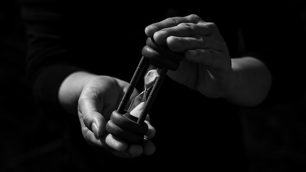 Business man holding a classic wood hourglass in the dark. thinking and control timing ideas concept.