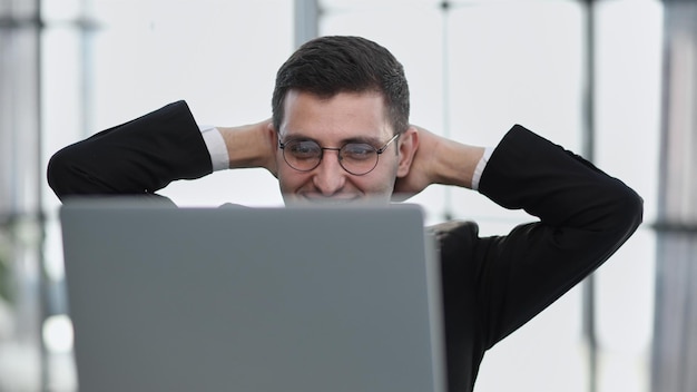 Business man holding his hands behind his head while working on a laptop