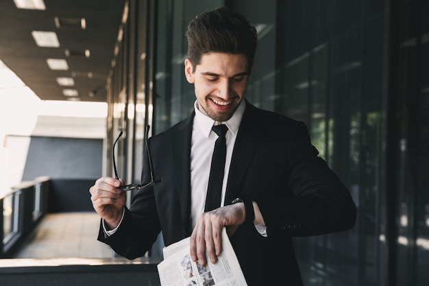 Business man near business center looking holding newspaper looking at watch.