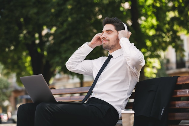 Business man outdoors in the park using laptop computer listening music.