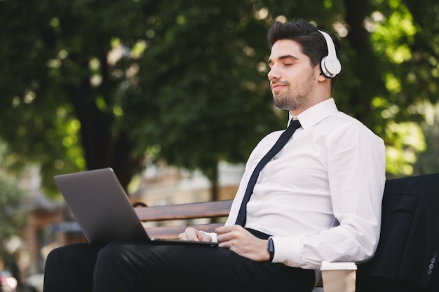 Business man outdoors in the park using laptop computer listening music.