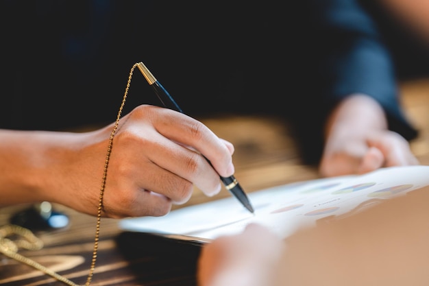 Business man person using a pen to sign a agreement document paper to approve by signature hand of businessman working on finance lawyer contract paperwork in office concept of deal on business desk