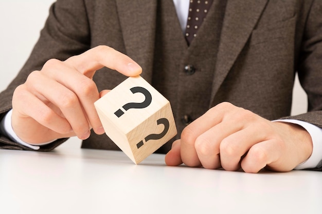 A business man's hand holds a wooden cube block with question marks on the corner concept of financial rating and mortgage rates