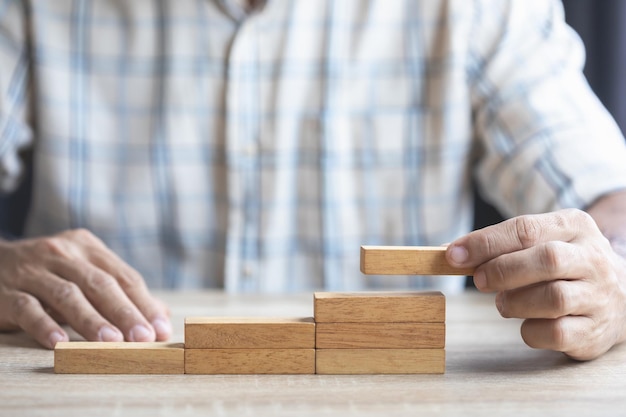 Business man's hand is stacking brown wooden block from low to higher Concept of strategy in business to make success