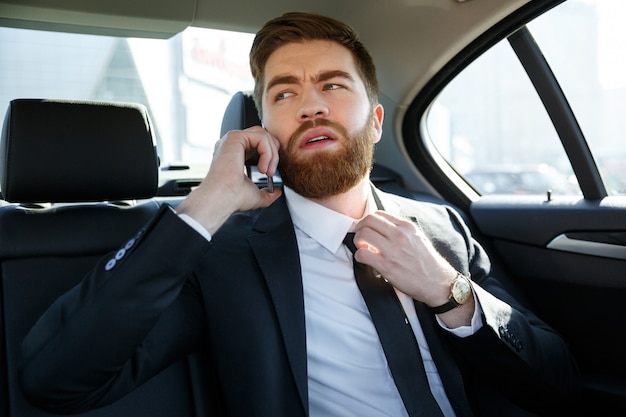 Business man talking on mobile phone and touching his necktie