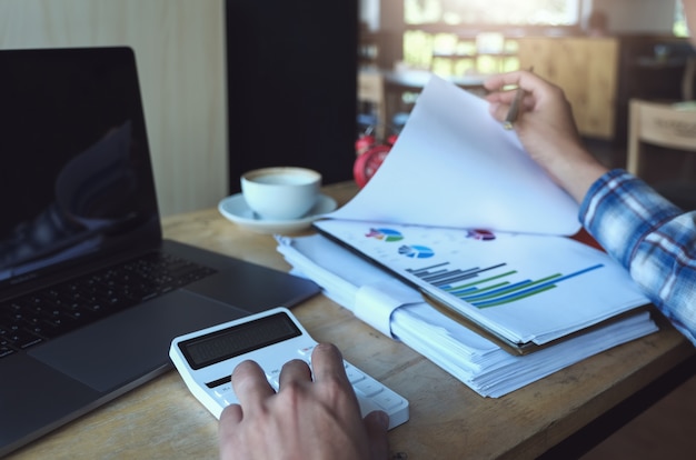 Business man using calculator to review balance sheet annual with holding pen and using laptop computer 