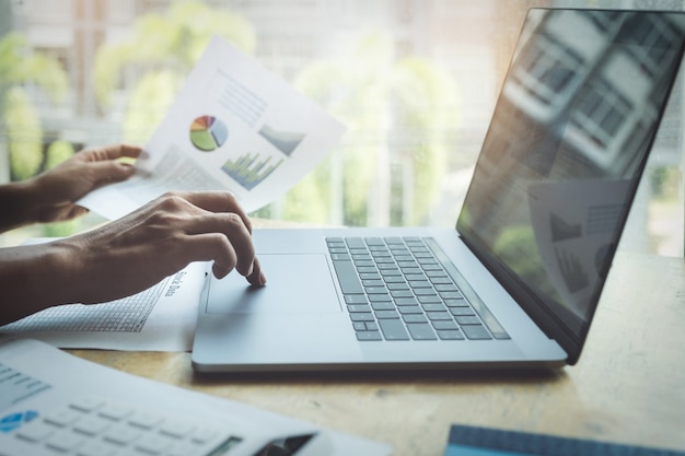 Business man using calculator to review balance sheet annual with using laptop computer to calculating budget.