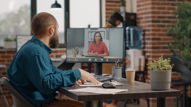 Business man using video call to talk to woman on computer in startup office. Entrepreneur meeting with manager on online video conference to discuss about project planning and strategy